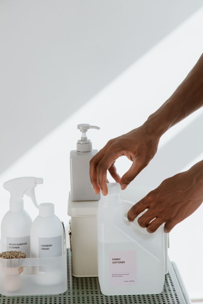 portfolio-01 Close-up of hands organizing various cleaning products on a white surface, showcasing cleanliness and home care essentials.