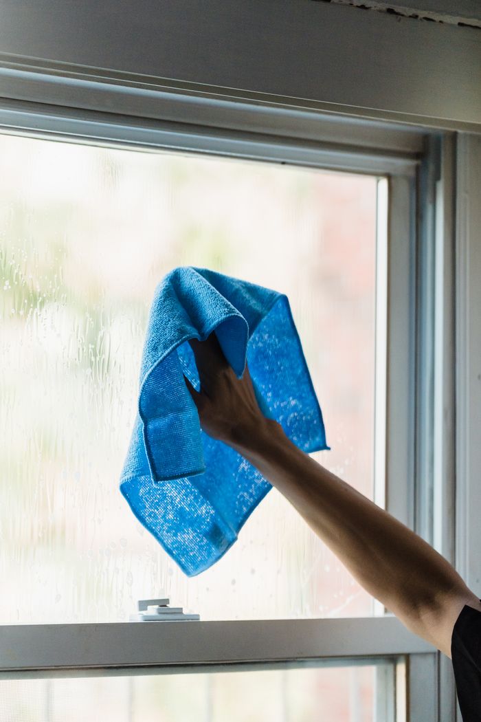 portfolio-03 A hand using a blue towel to clean a window indoors, showcasing housework.