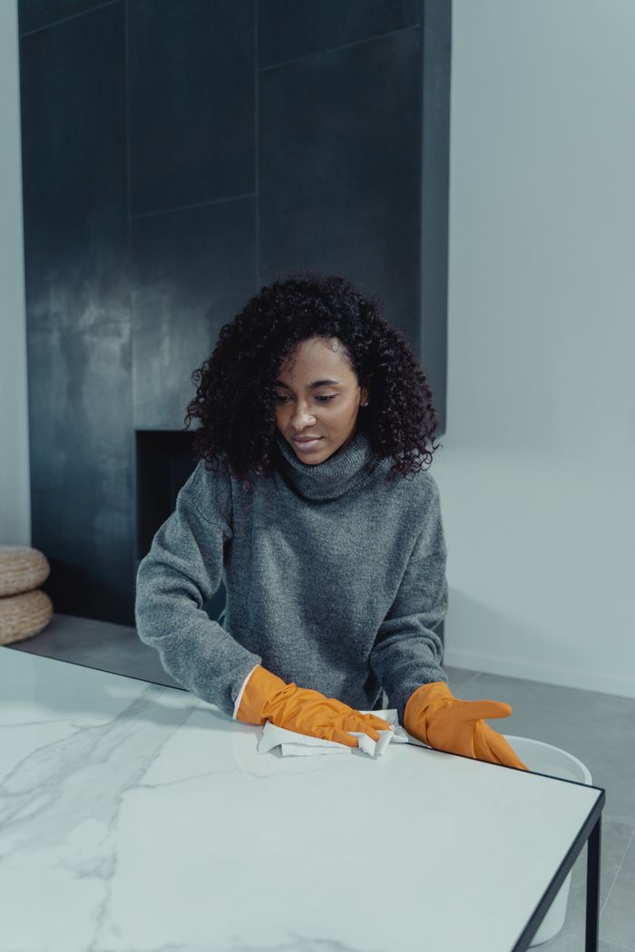 portfolio-02 A woman wearing gloves cleans a marble table in a modern indoor setting, focusing on cleanliness and hygiene.
